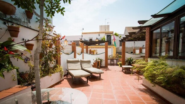 Una terraza en la azotea con dos sillones, una mesa de vidrio y baldosas de terracota.