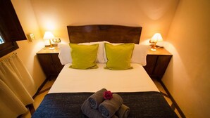 Una cama bien hecha con dos almohadas verdes, un cabecero de madera y dos lámparas de noche.