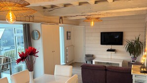 A modern living room with a dining area, wooden beams on the ceiling, a flat-screen TV, and a potted plant. - La Petite Chaumière de Pentrez, sea view (Saint-Nic)