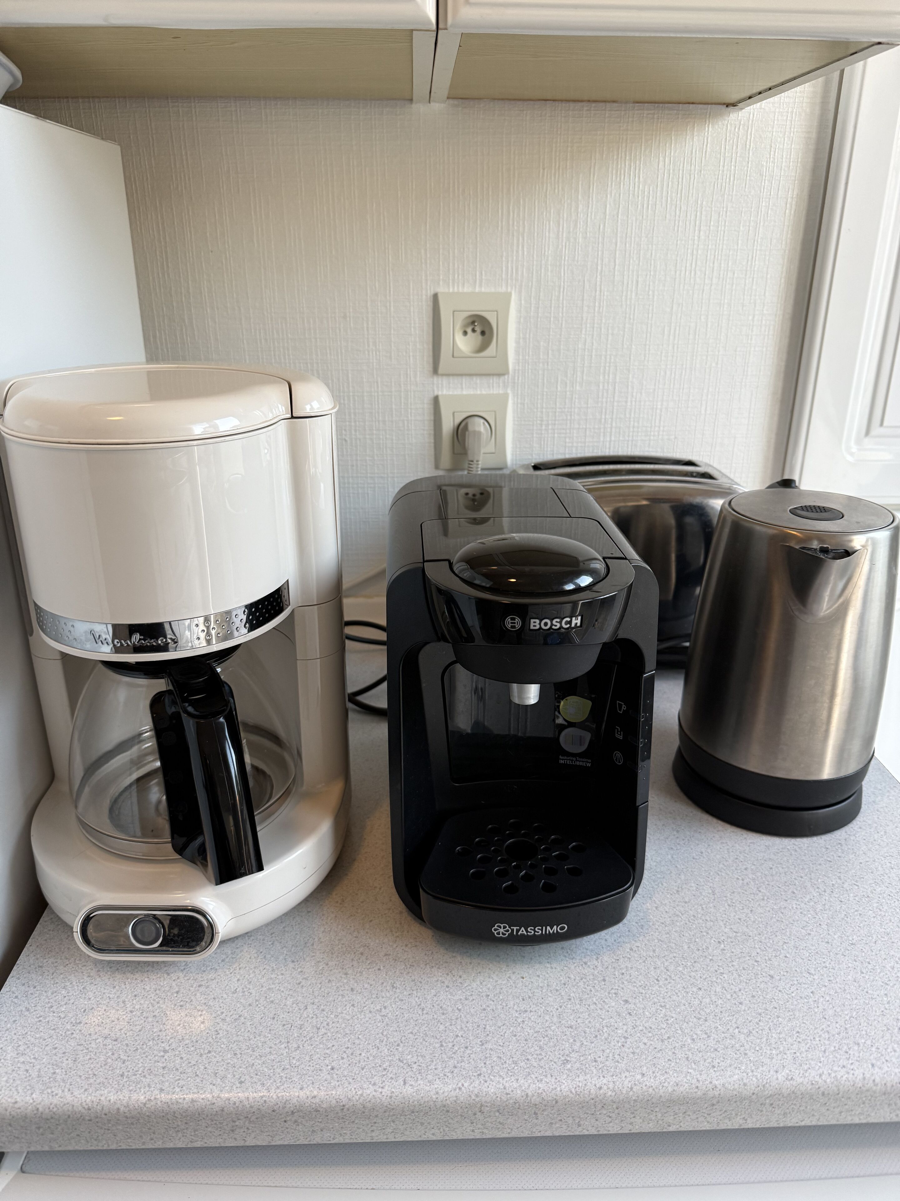 A kitchenette with a coffee maker, a toaster, and a kettle on a countertop.