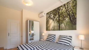 Een slaapkamer met een bed, nachtkastjes, een kledingkast en een groot raam met uitzicht op bomen.
