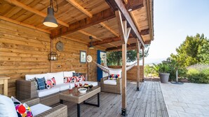 Een houten terras met een bank en tafel, een hangmat, en uitzicht op de omgeving.