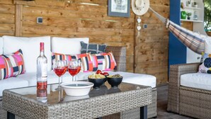 Een gezellig houten blokhutinterieur met een rieten bank, een eettafel met een fles wijn en glazen, en een hangmat.