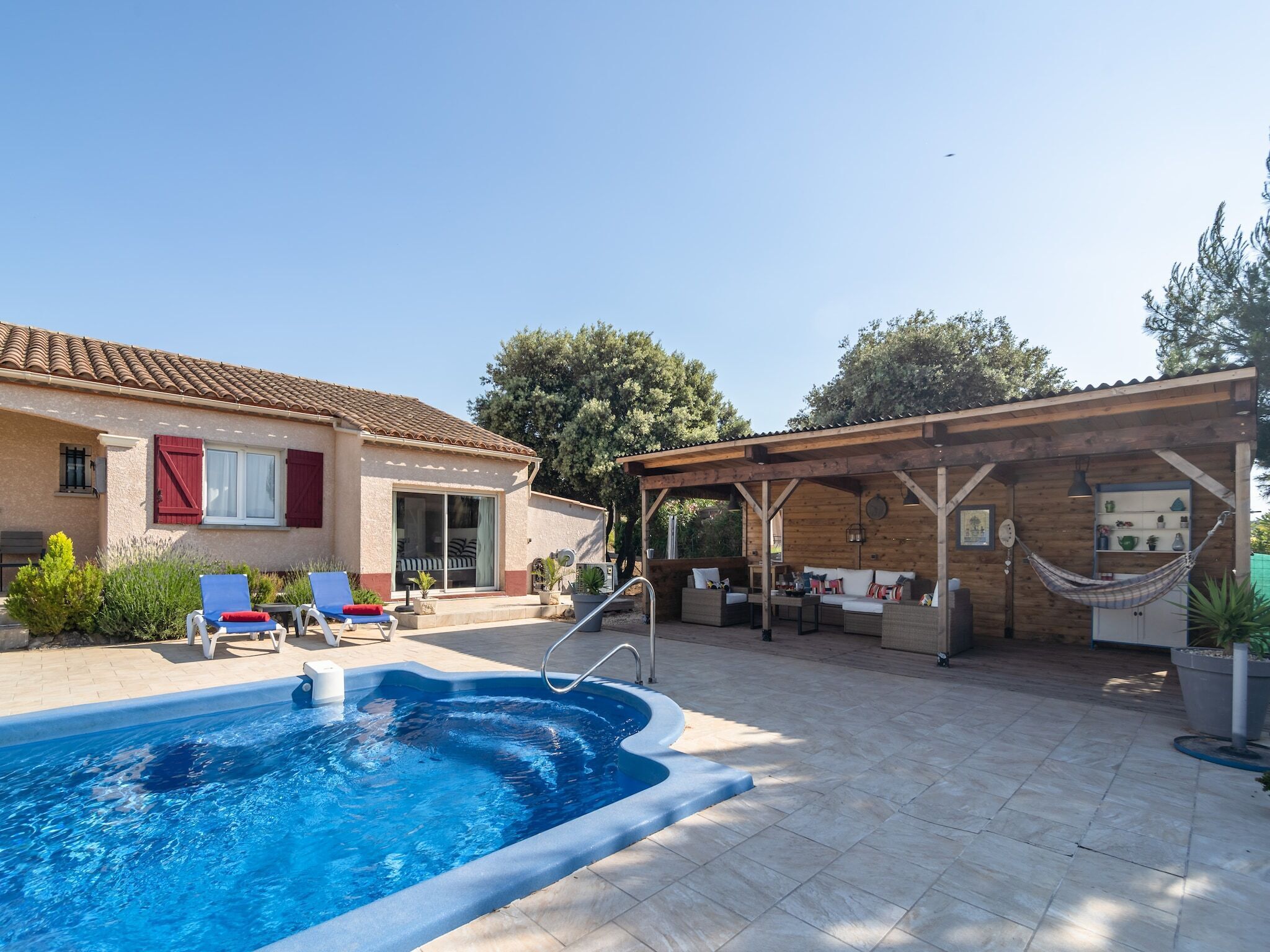 A pool area with a covered seating area, a building with red shutters, and a hammock.