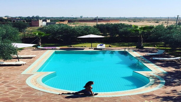 Piscina rectangular con borde de azulejos, rodeada de sillas de descanso y sombrillas.