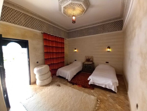 Une chambre avec deux lits, un rideau rouge, un plafond à motifs et un petit placard.