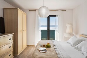Un dormitorio con cama, armario, televisor y vista al mar a través de un ventanal grande.