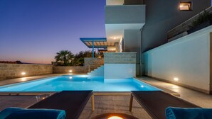 A pool area with lounge chairs and a candle, surrounded by a modern building with a staircase leading to an upper level. - Villa Allegra with 32msq heated pool, 300m far from sandy beaches, open sea view (Duce)