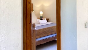 Un chambranle de porte en bois mène à une chambre à coucher qui contient un lit, une table de chevet, une lampe et un tableau encadré accroché au mur.