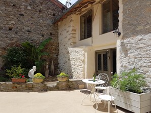 A stone building with a white exterior, a small garden area with potted plants, and a white outdoor seating area with metal chairs and a table. - Luxury loft in rural Pyrenees village-relax, walk, cycle, birdwatch, chill, wifi (Soueich)