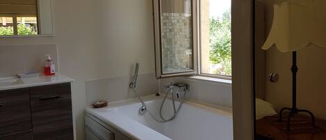 A bathroom with a white sink, a mirror, a window, and a wooden floor.