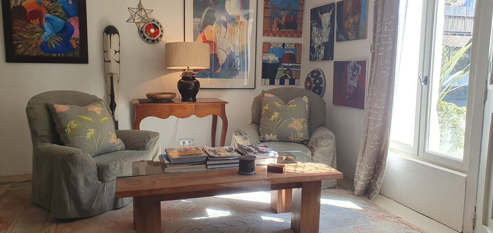 A cozy living room with two armchairs, a wooden coffee table, and various artworks on the walls.