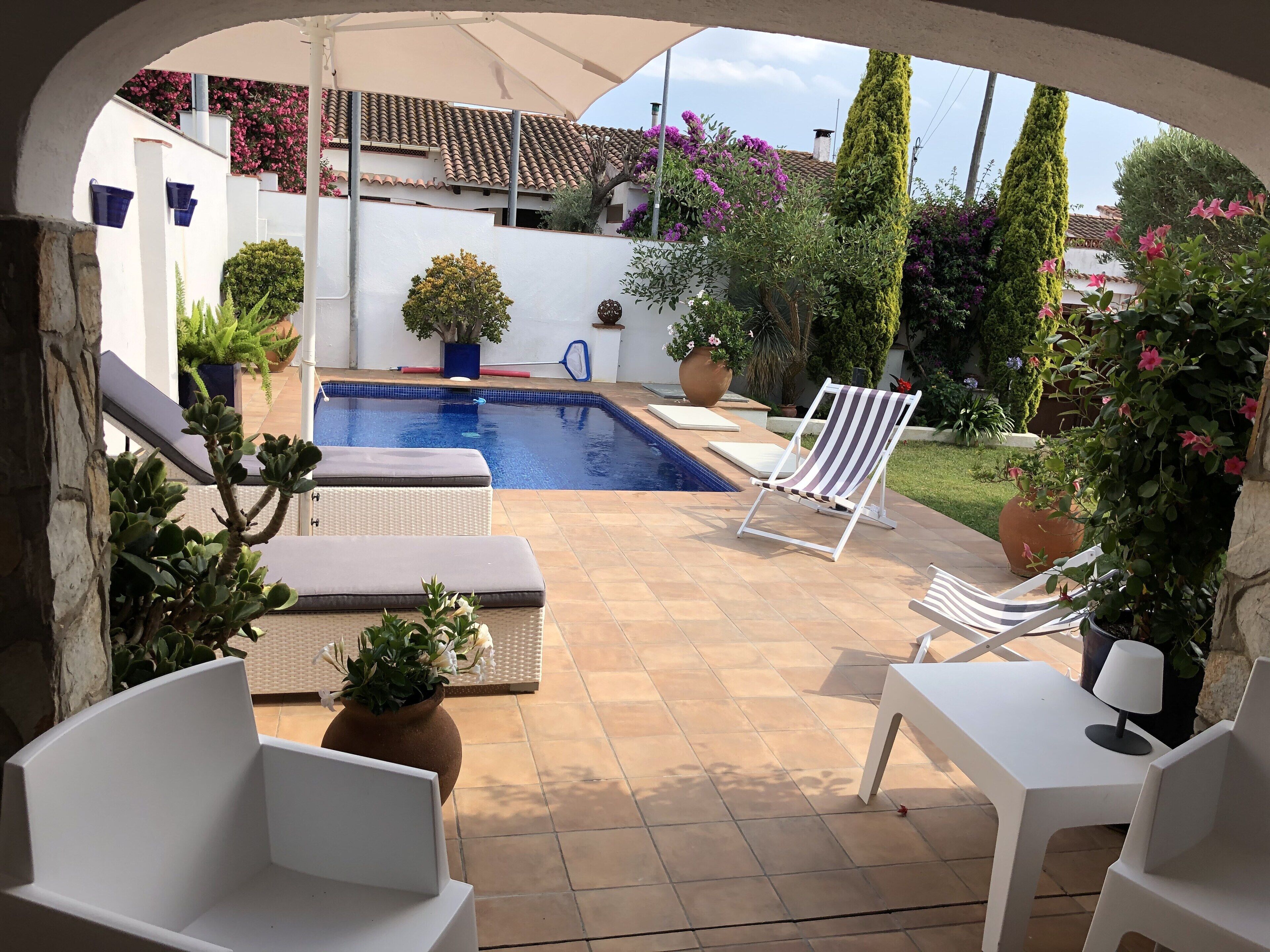 A pool area with a tiled deck, lounge chairs, and potted plants.