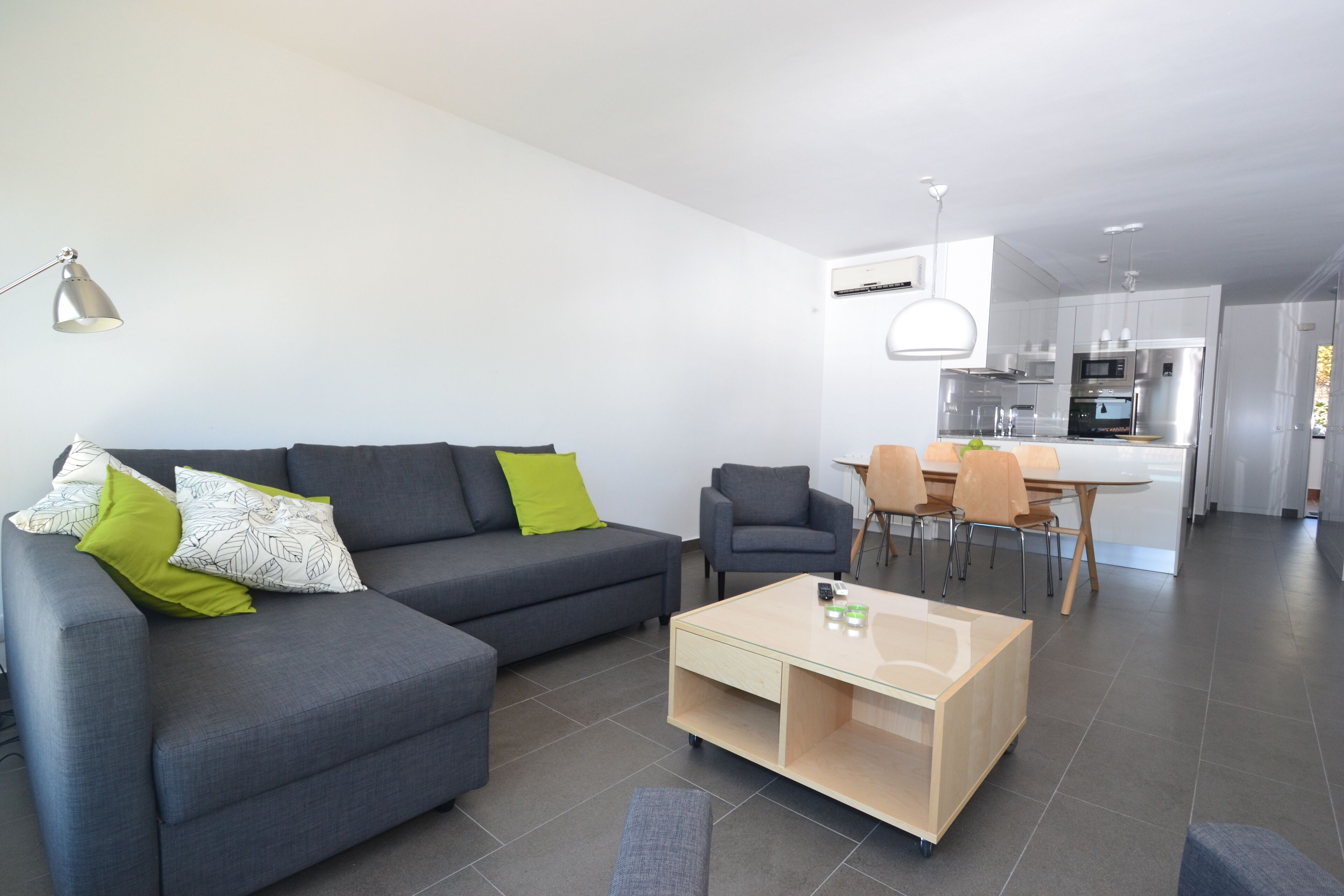 A modern living room with a grey sofa, a wooden coffee table, and a dining area with chairs and a table.