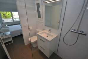 Une salle de bain moderne avec une douche à l’italienne en verre, un lavabo blanc et un grand miroir.