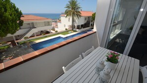 Un balcón con una mesa blanca, una piscina pequeña y vistas al mar y edificios.