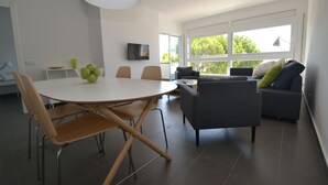 Una sala de estar moderna con una mesa de comedor redonda, dos sillas, un sofá y un televisor montado en la pared.