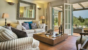A living room with a sofa, coffee table, and a large mirror. There is a window with curtains and a view of greenery outside. - 'Phivos Villa'Elegant Villa With Dramatic Mountain & Sea Views, Totally Equipped (Kefalonia)