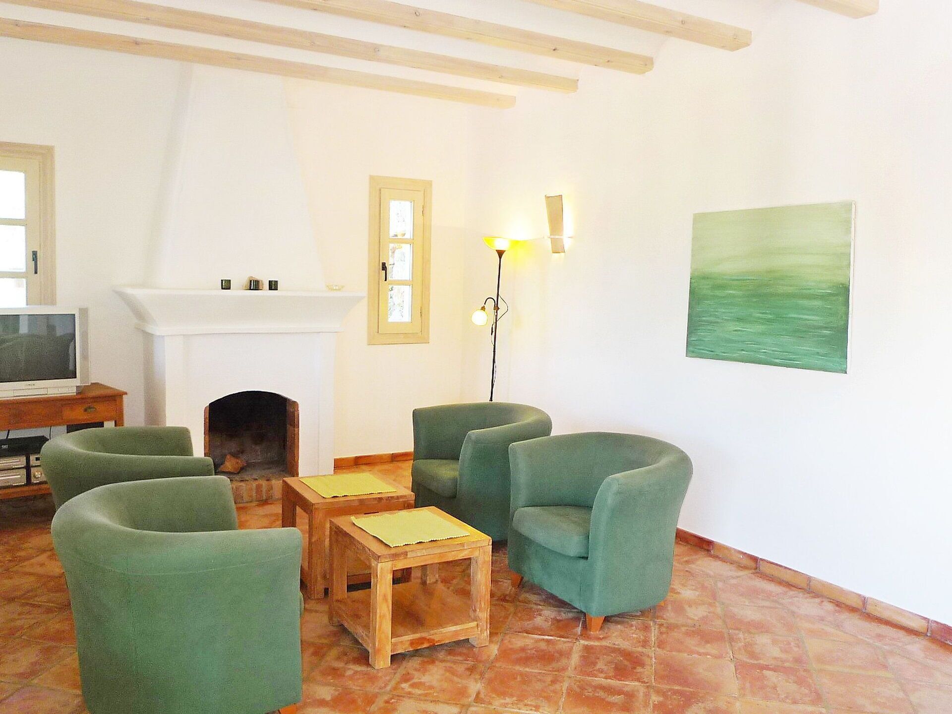 A living room with green armchairs, a fireplace, a TV, and a painting on the wall.
