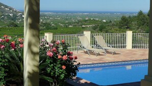 Zona junto a la piscina con vistas al mar y colinas.