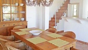 Un comedor con mesa de madera, sillas de mimbre, una araña y una escalera.