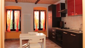 A kitchen with a white table, red cabinets, and a window with orange curtains.