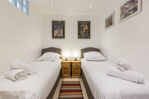 A hotel room with two beds, a striped rug, and two nightstands with lamps.