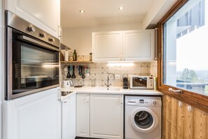 A compact kitchen with white cabinets, a built-in oven, a microwave, a sink, and a Bosch washing machine.