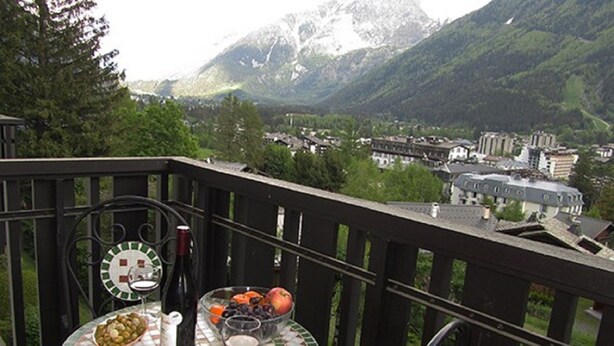 A balcony with a table set for a meal, featuring a bottle, a bowl of olives, a bowl of fruit, and a plate of cheese. - Le Pied du Brevent -  a studio that sleeps 4 guests (Chamonix)