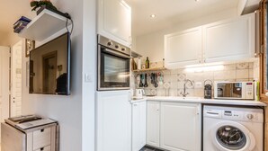 A compact kitchen with white cabinets, a built-in oven, a microwave, and a washing machine. - Le Pied du Brevent -  a studio that sleeps 4 guests (Chamonix)
