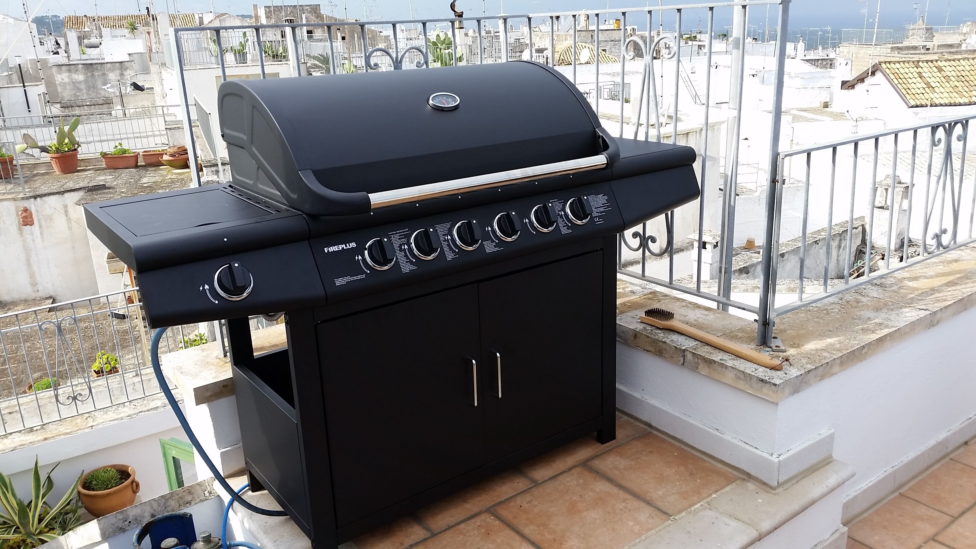 En svart utomhusgrill med en digital display, placerad på en balkong med utsikt över stadsbilden.