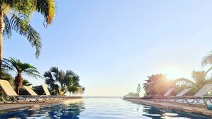 An infinity pool with clear blue water, surrounded by palm trees and lounge chairs, under a clear sky. - Bay View Villa Cyprus, Luxury at its finest!! (Protaras)