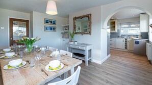 Un coin repas avec une table en bois dressée pour le repas, un miroir au mur et une cuisine en arrière-plan.