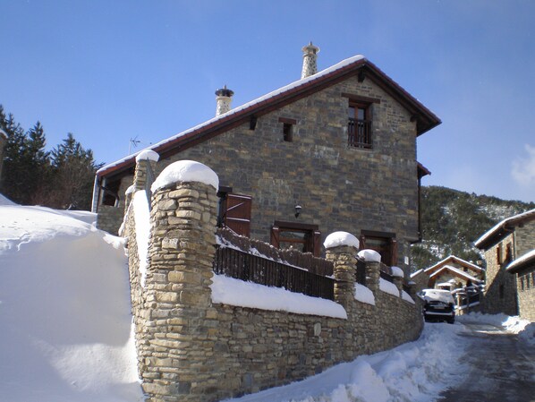 A stone building with a snow-covered roof and chimney, surrounded by snow.