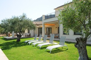 A modern villa with a covered outdoor seating area, a pool, and a well-maintained lawn.
