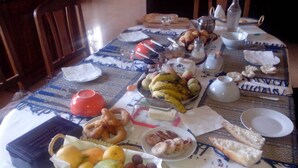 Mesa de comedor servida con diversas comidas y bebidas, entre ellas frutas, pan y una botella.