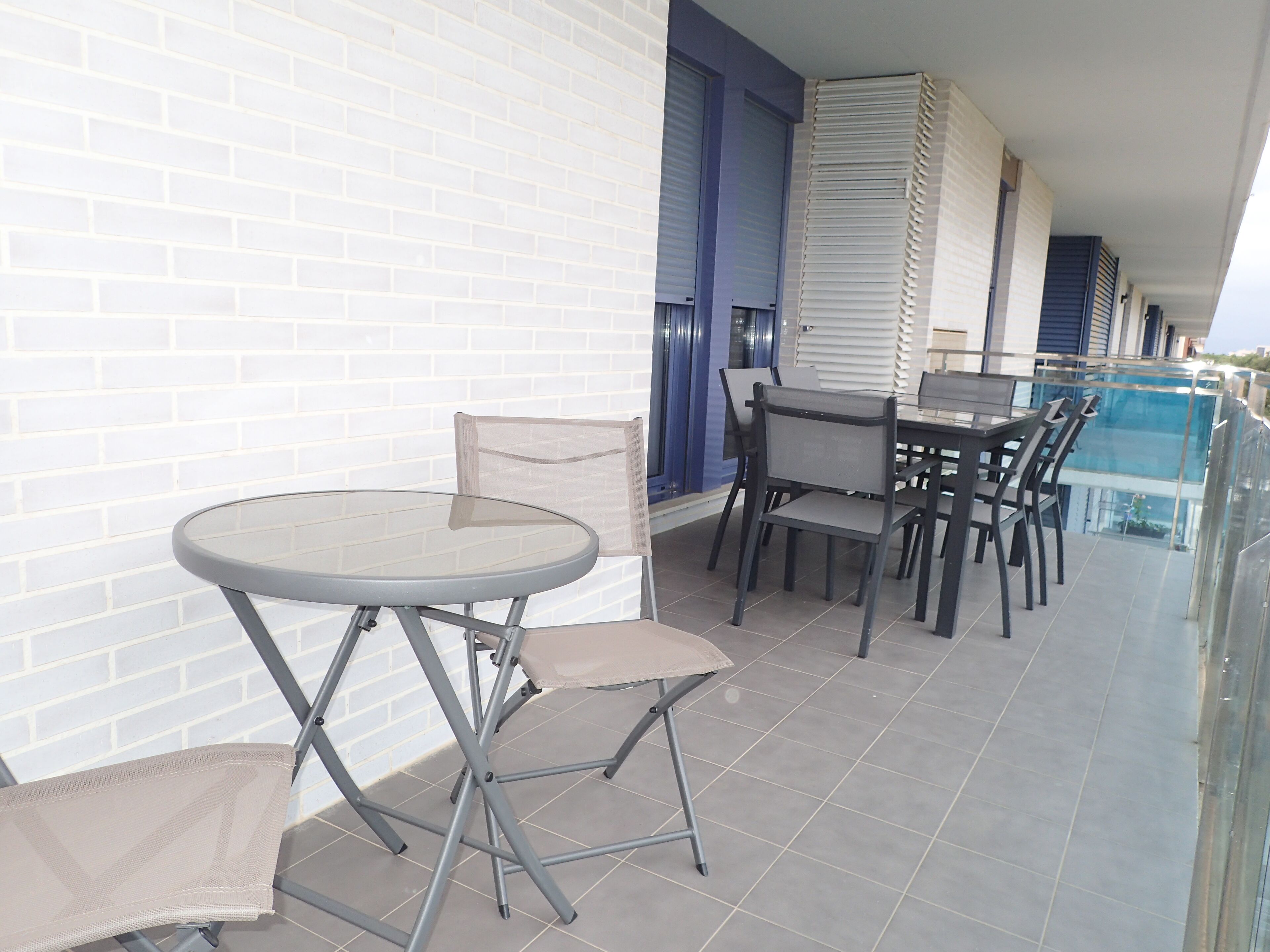 A balcony with a round table and chairs, a glass railing, and a view of the pool.