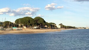 A coastal scene with a sandy beach, calm sea, and a row of trees and buildings along the shore. - 2 APARTMENT WITH POOL IN FRONT OF ESQUIROL DE CAMBRILS BEACH (Cambrils)