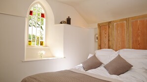 Ein Schlafzimmer mit einem großen Bogenfenster, einem hölzernen Kopfteil und einem Bett mit weißen Leinen und braunen Kissen.