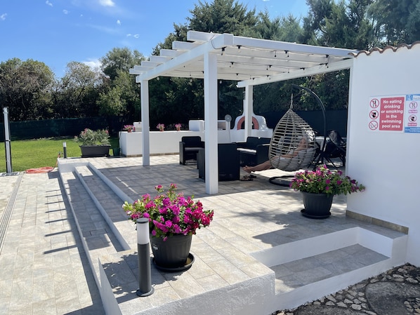 Un espacio exterior cubierto con una pérgola, mobiliario para exteriores y plantas en macetas.