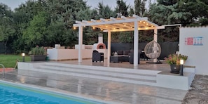 Un patio al aire libre con pérgola, mobiliario y zona de barbacoa.