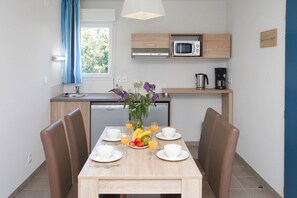 A modern kitchen with a microwave, coffee maker, and a small dining area with a table set for two. - Apartment in Bretagne near Morbihan Coast (BADEN)