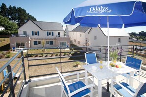 A terrace with a table set for dining, blue chairs, and a blue umbrella with 'Odaly's Vacances' branding.
