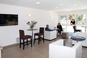 A modern waiting area with white furniture, a flat-screen TV, and a window with a view of the outdoors.