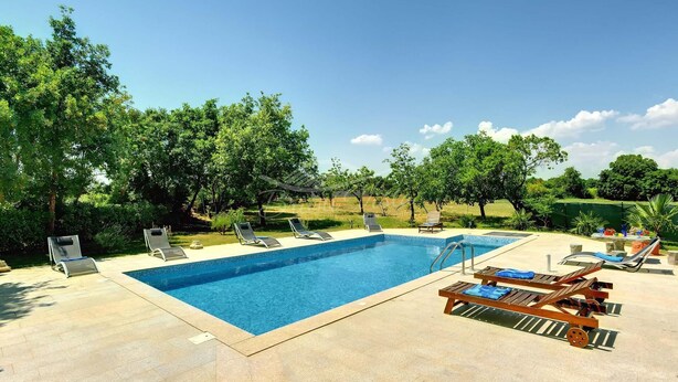 Une piscine rectangulaire, bordée d’une terrasse carrelée, entourée de chaises longues et agrémentée d’une pergola.