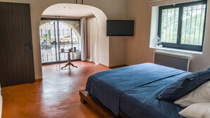 A bedroom with a bed, a TV mounted on the wall, and a window with a view of greenery. - Old barn renovated to nine  (BAGNOLS SUR CÈZE)