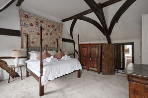 A four-poster bed with white linens, a wooden nightstand with a lamp, and a large tapestry on the wall. - Cotswolds home in Castle Combe (optional Hot Tub) (Castle Combe)