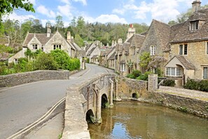 A stone bridge over a narrow waterway, connecting two rows of traditional stone houses with pitched roofs. - Cotswolds home in Castle Combe (optional Hot Tub) (Castle Combe)