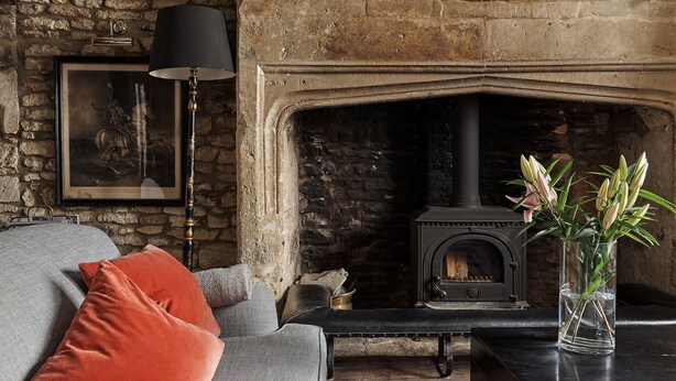 A cozy living room with a stone wall, a fireplace, a sofa with cushions, and a vase with flowers on a table. - Cotswolds home in Castle Combe (optional Hot Tub) (Castle Combe)