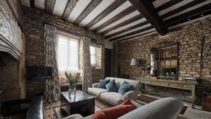 A rustic living room with exposed stone walls, a wooden ceiling, a sofa set, a coffee table, and a television. - Cotswolds home in Castle Combe (optional Hot Tub) (Castle Combe)